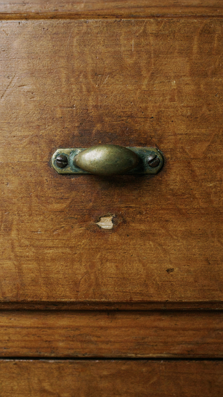 A close-up of an old wooden dresser drawer handle with genuine wear and fading.