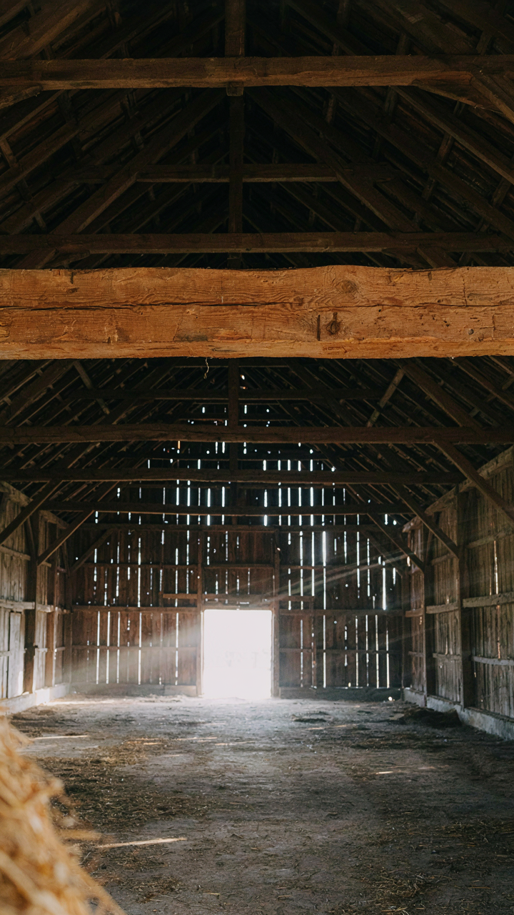 A massive, uninsulated timber beam crosses a wide, empty barn interior.