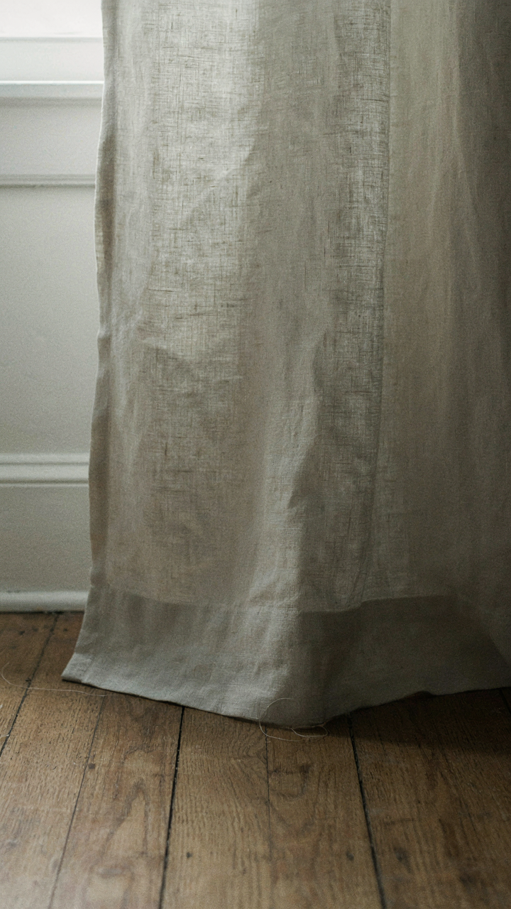 Close-up of a textured raw linen curtain and unfinished wooden floor.