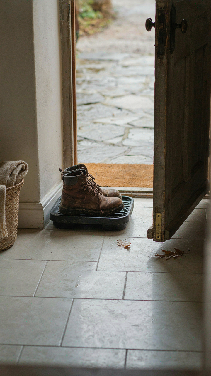 A rubber boot tray just inside a cottage mudroom door on sealed tile, holding muddy boots.