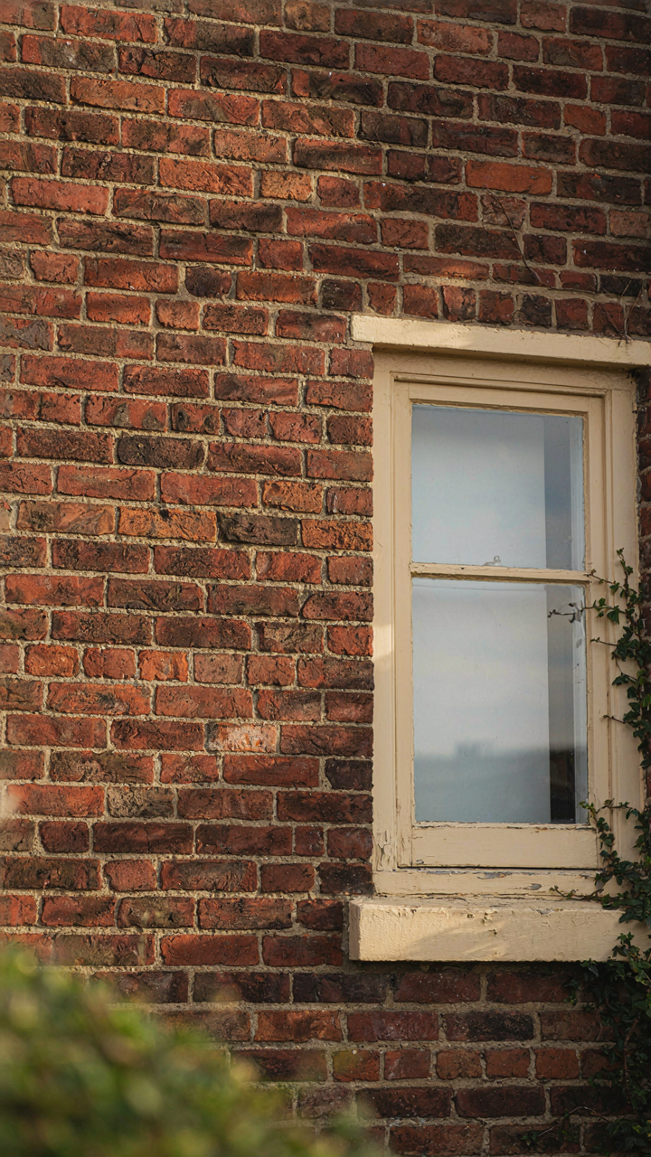 Red brick bungalow wall with cream trim around a window.