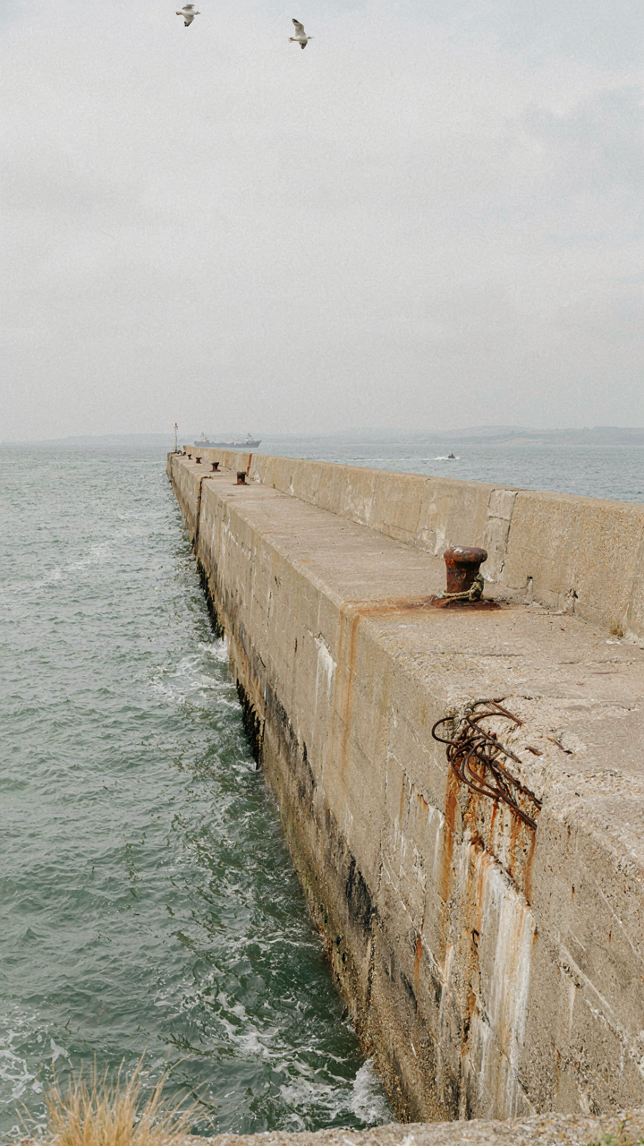 Brutalist concrete pier extending into a choppy harbor, showing exposed rebar and concrete.