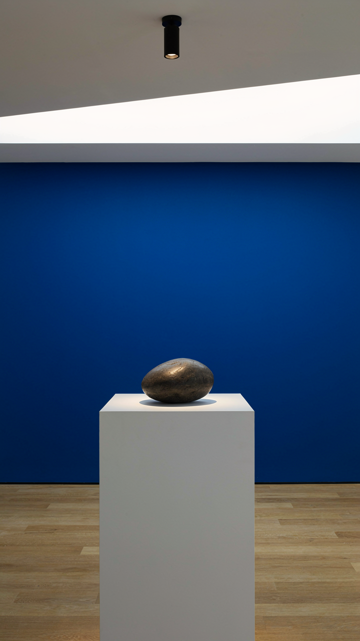 A single smooth river stone sits on a white pedestal in a minimalist art gallery.