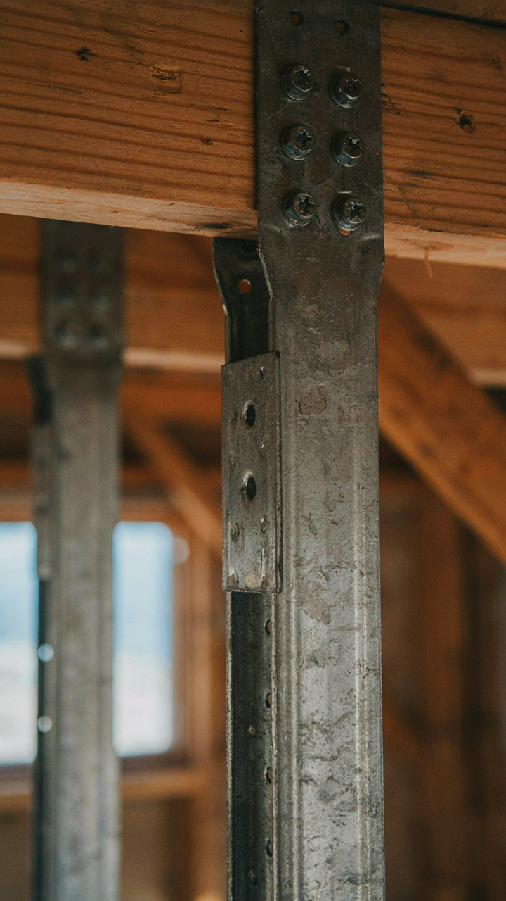 Close-up of galvanized steel joist hangers and fasteners on a wood beam.
