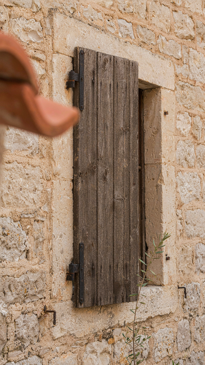 A thick, weathered wooden shutter securely closed over a window on a stone wall.