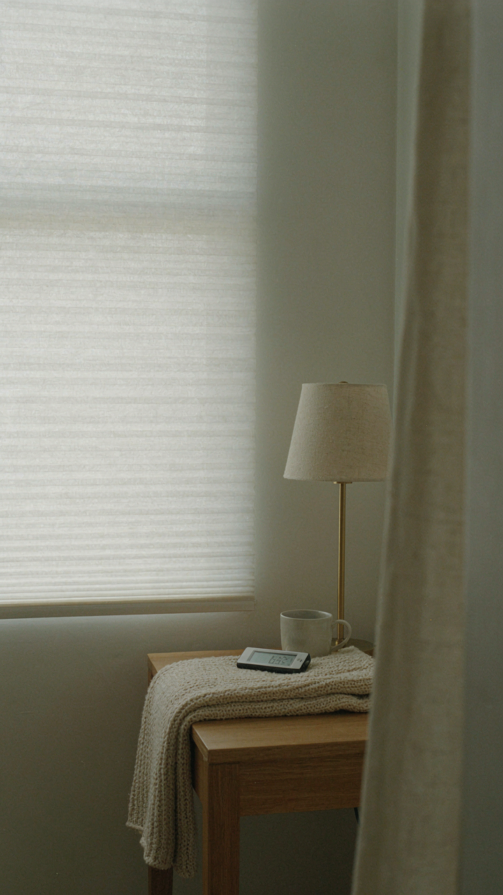 Bedroom window with cellular shades down and a warm-spectrum light glowing.