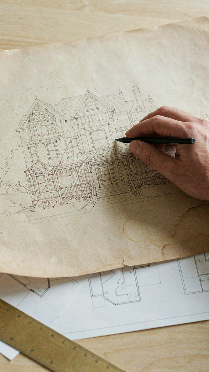 A hand tracing an old blueprint next to a new architectural drawing.
