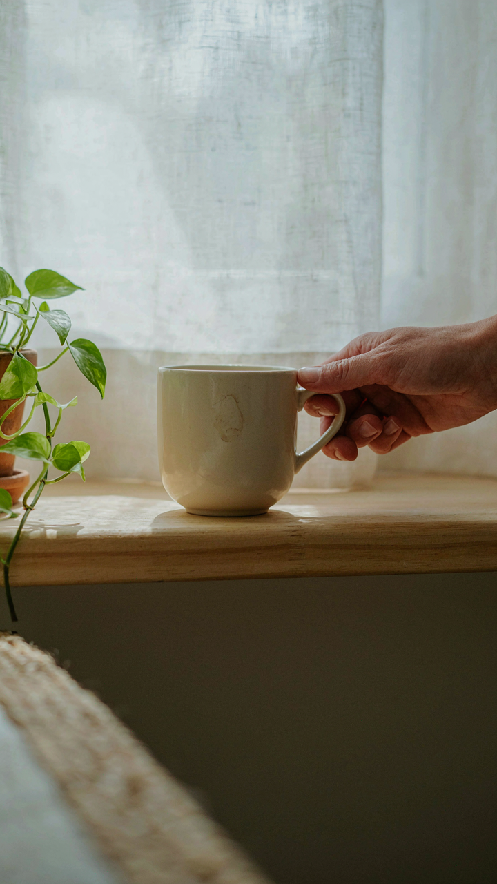 A hand places a ceramic mug on a clean wooden shelf in a small room.