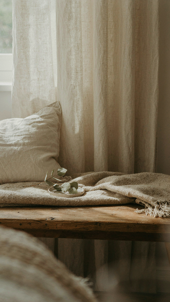 Layered textiles of cream linen, wool, and cotton in harmonious neutral tones on a bench.