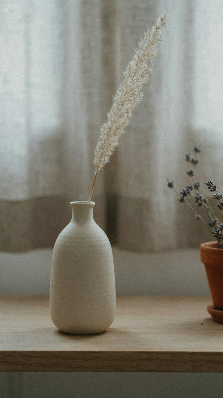 A ceramic vase with a dried flower on a clean shelf.