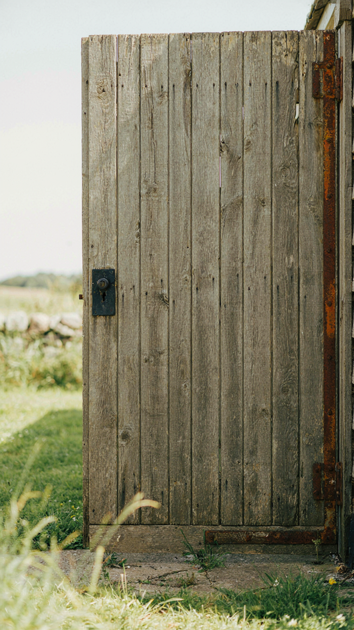 A weathered wooden shed door with authentic graying patina and oxidized metal hardware.