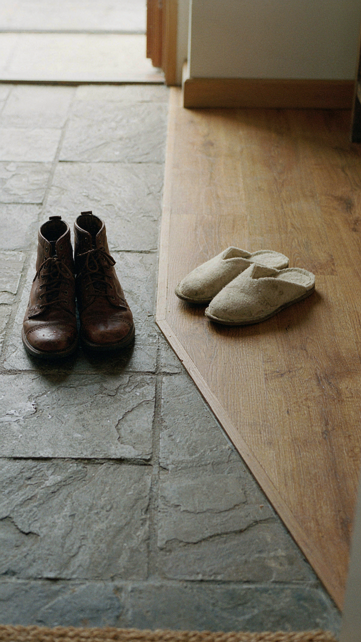 Rough stone floor meets polished wood in a cottage entry, separating wet boots from clean slippers.