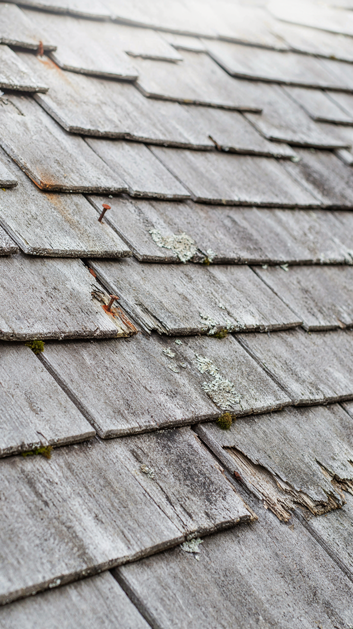 A close-up of a neglected cottage roof with weathered and damaged cedar shingles.