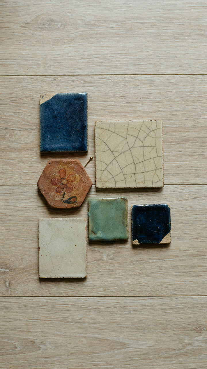 A collection of intentionally mismatched antique ceramic tiles on a wooden surface.