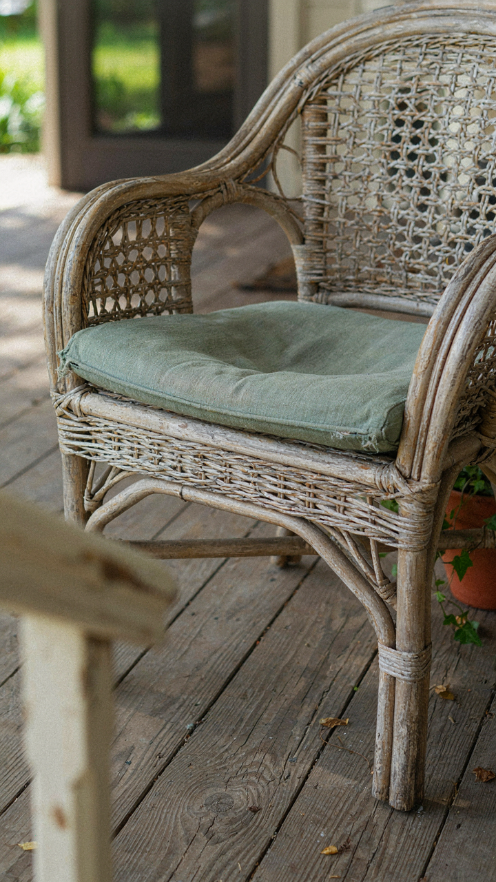 A vintage wicker chair on a cottage porch shows a worn spot from frequent use.
