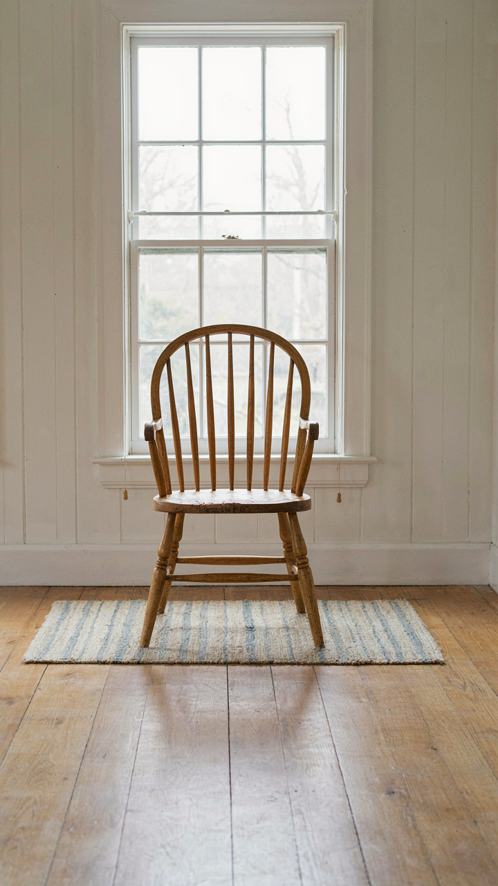 A single antique Windsor chair in a bright, empty room.