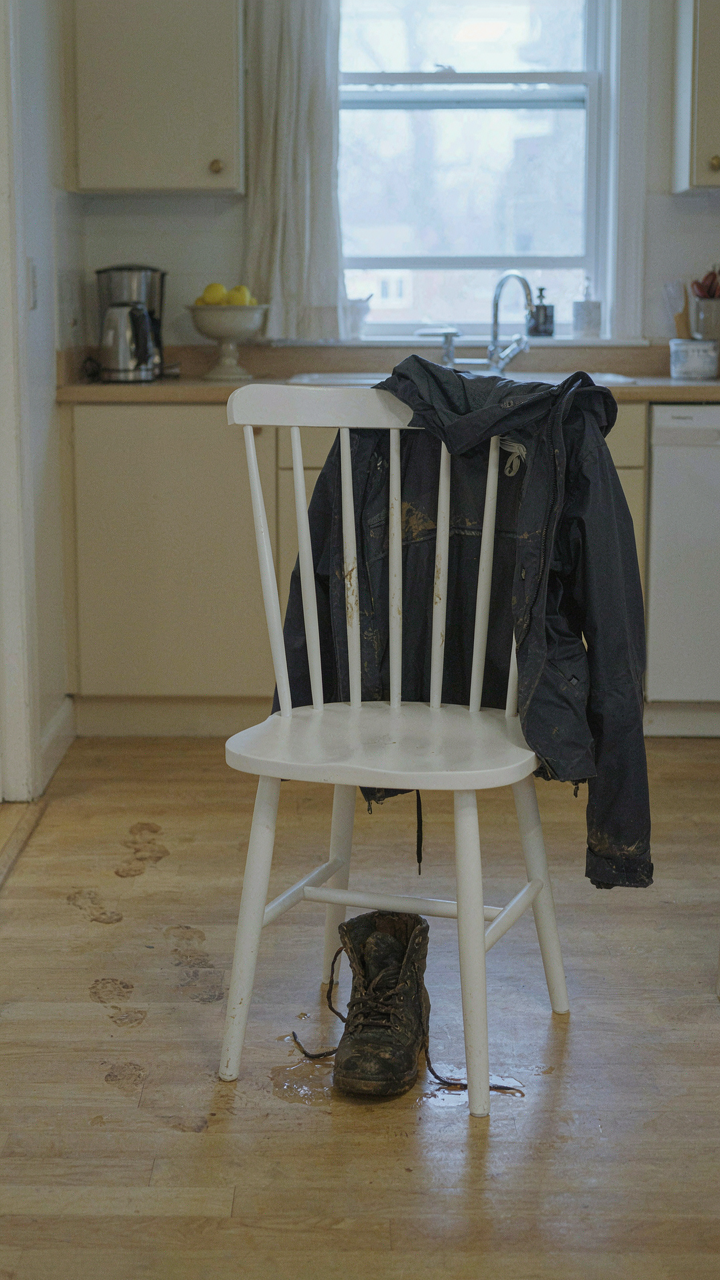 A muddy jacket on a kitchen chair, showing chaos bleeding from the entryway.