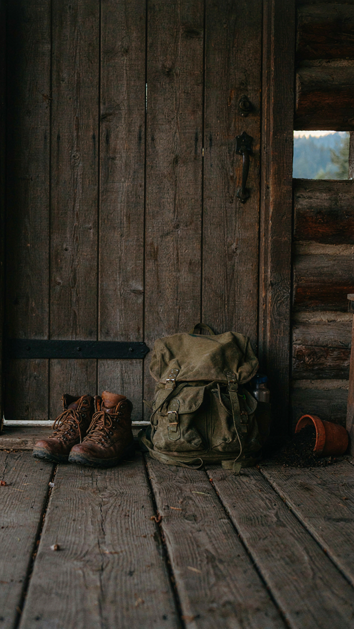 Muddy hiking boots and a backpack rest on a wooden wraparound porch.