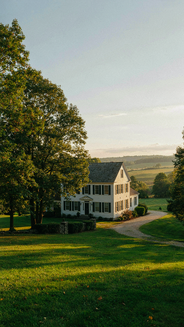 A colonial revival house with windows facing the setting sun, surrounded by trees.