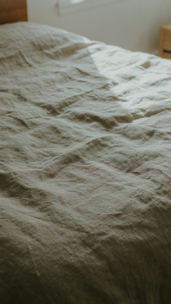 A close-up of a faded and worn linen duvet cover on a bed, showing intentional imperfection.
