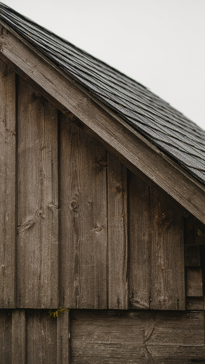 A rustic garden shed's exterior wall shows gapped boards and a steep roofline.