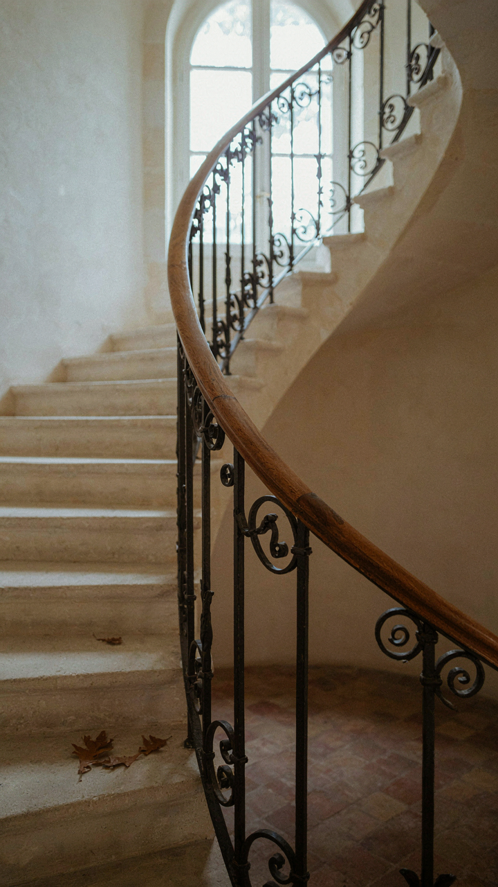 An eye follows the smooth curve of a French country staircase's iron railing.