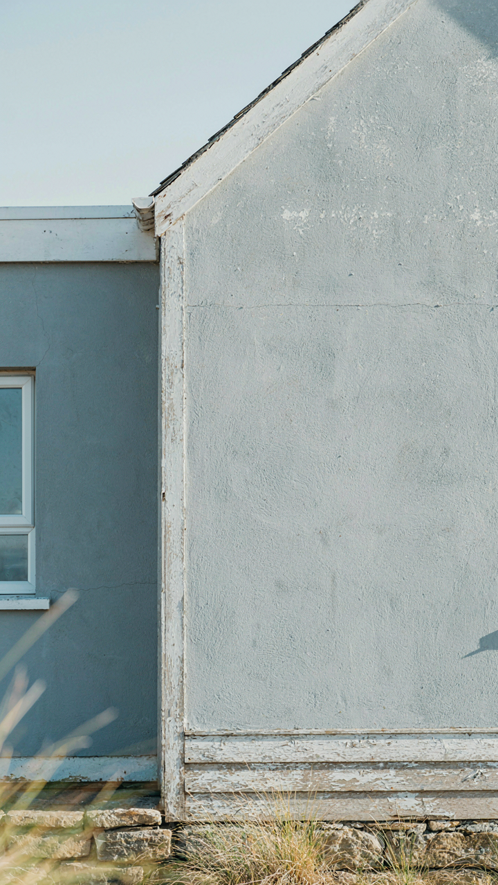 A sunlit light gray wall on a coastal cottage next to a sheltered muted blue wall.