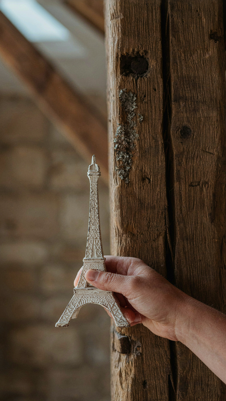 A hand holds a fake miniature Eiffel Tower next to a real weathered wood beam.