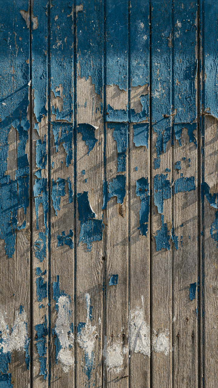 Close-up of peeling blue paint on a weathered wooden wall with salt residue.