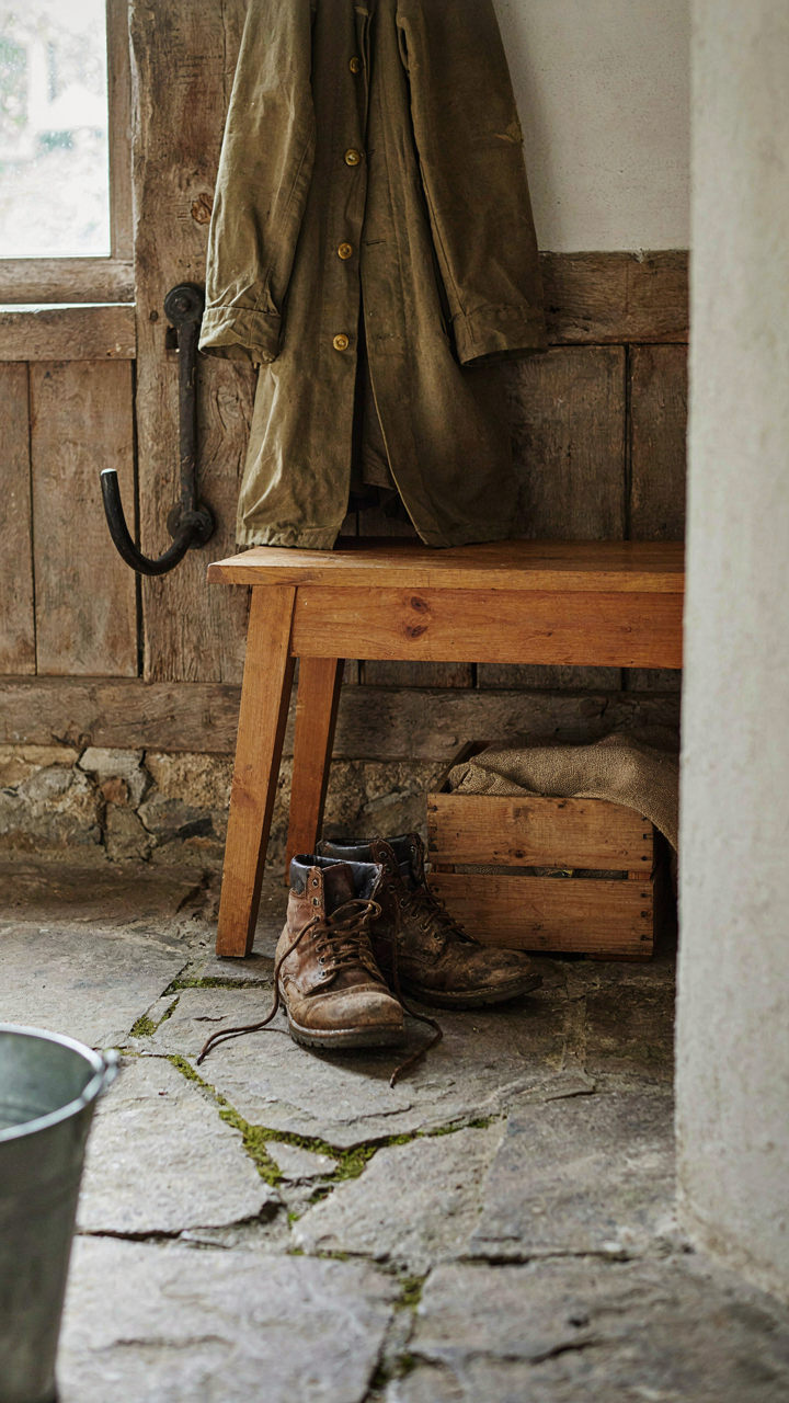 Muddy boots and a work coat on a stone floor in a functional french country entryway.