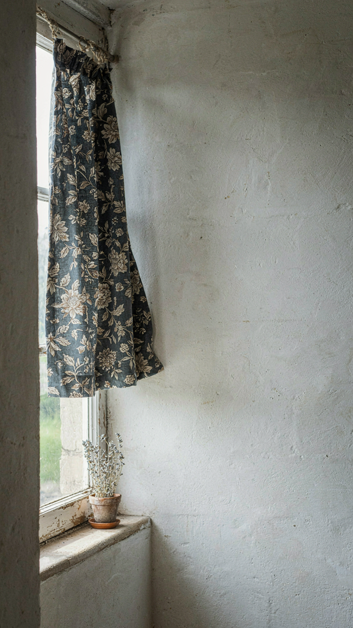 A single toile curtain panel against a plain whitewashed wall in a farmhouse.
