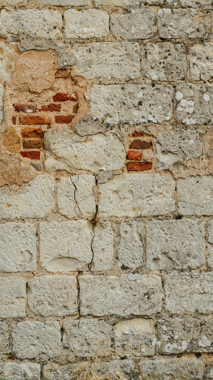 An old stone wall has weathered plaster, revealing brick underneath.