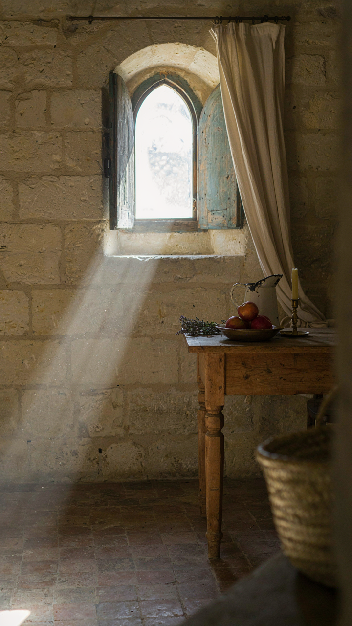 Sunlight streams through a small window in a thick stone wall of a French country cottage.