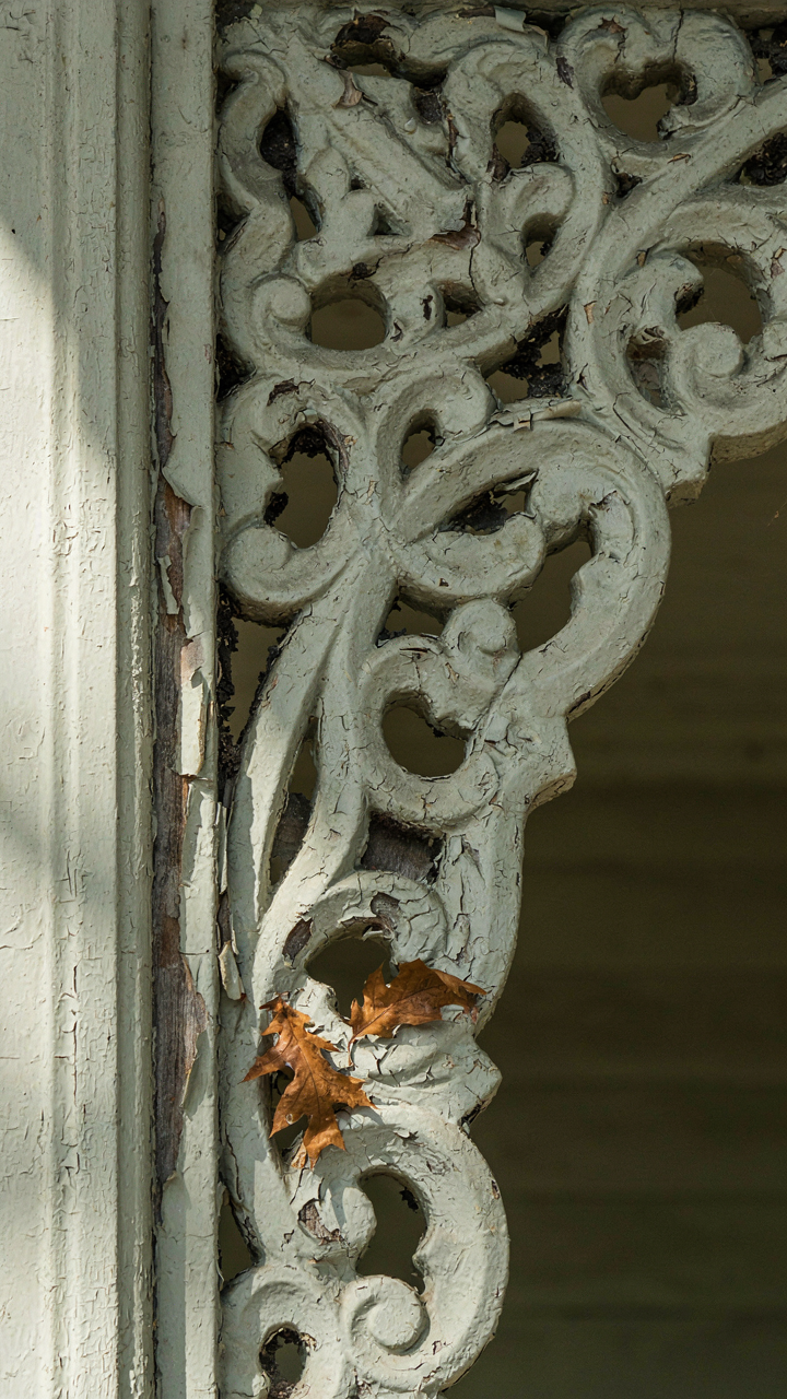 Close-up of a rotting victorian porch gingerbread trim with peeling paint.