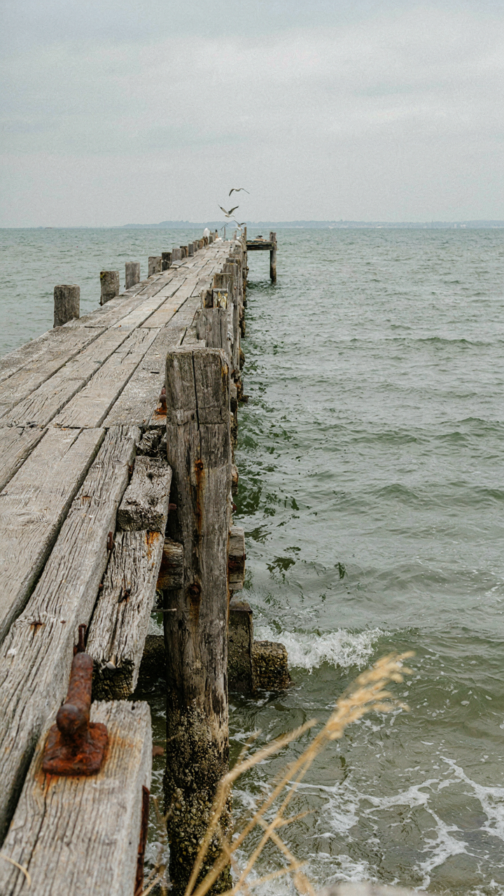 Weathered wooden dock extending into a choppy sea, showing salt erosion on pilings.