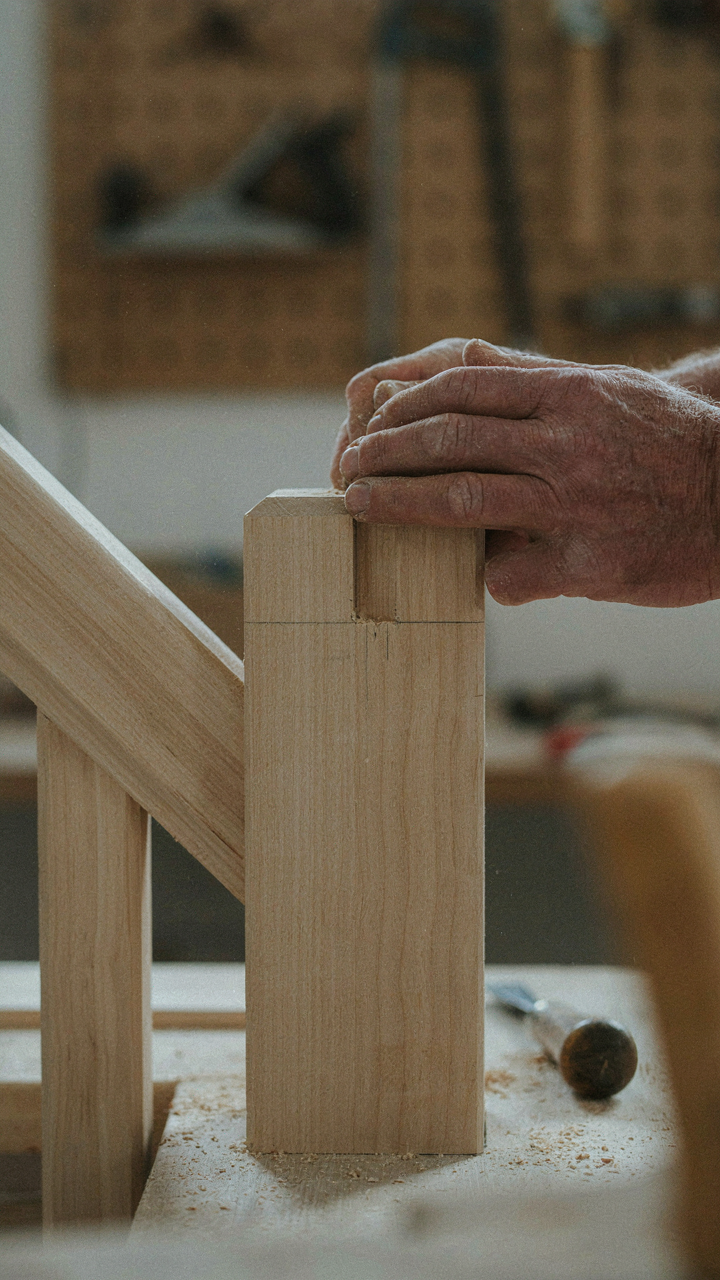 A carpenter's hands fitting a mortise and tenon joint on a newel post.
