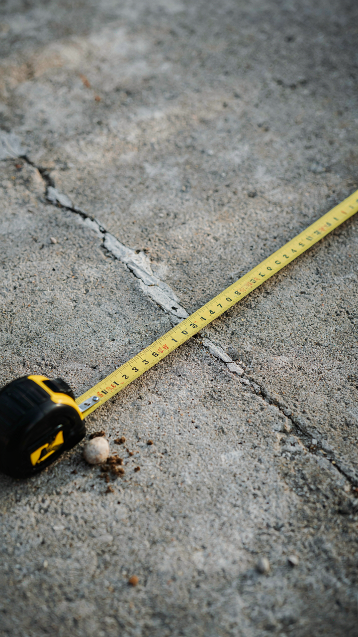 A small crack on a concrete foundation, being measured with a tape.