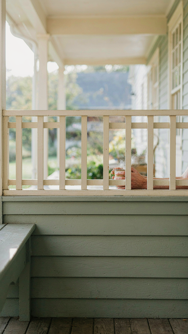 A ranch house porch railing with a knee wall and a person sitting on a low bench.