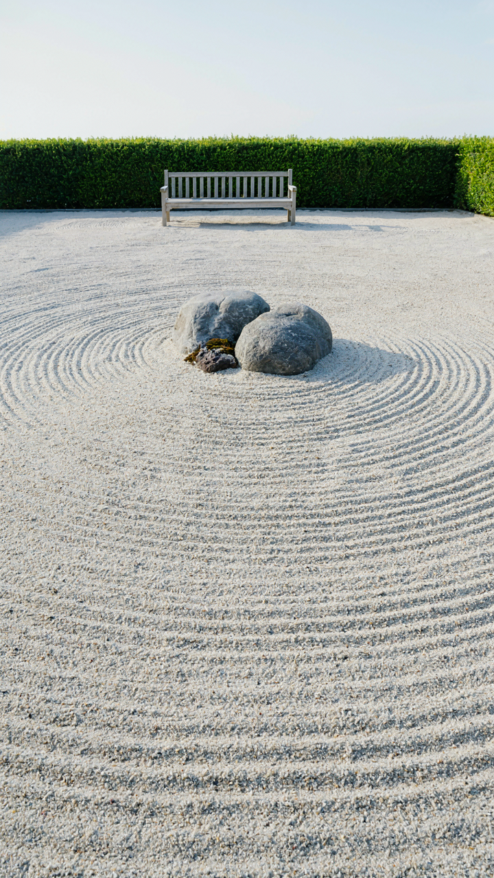 A tranquil Japanese rock garden with raked white sand and two grey stones.
