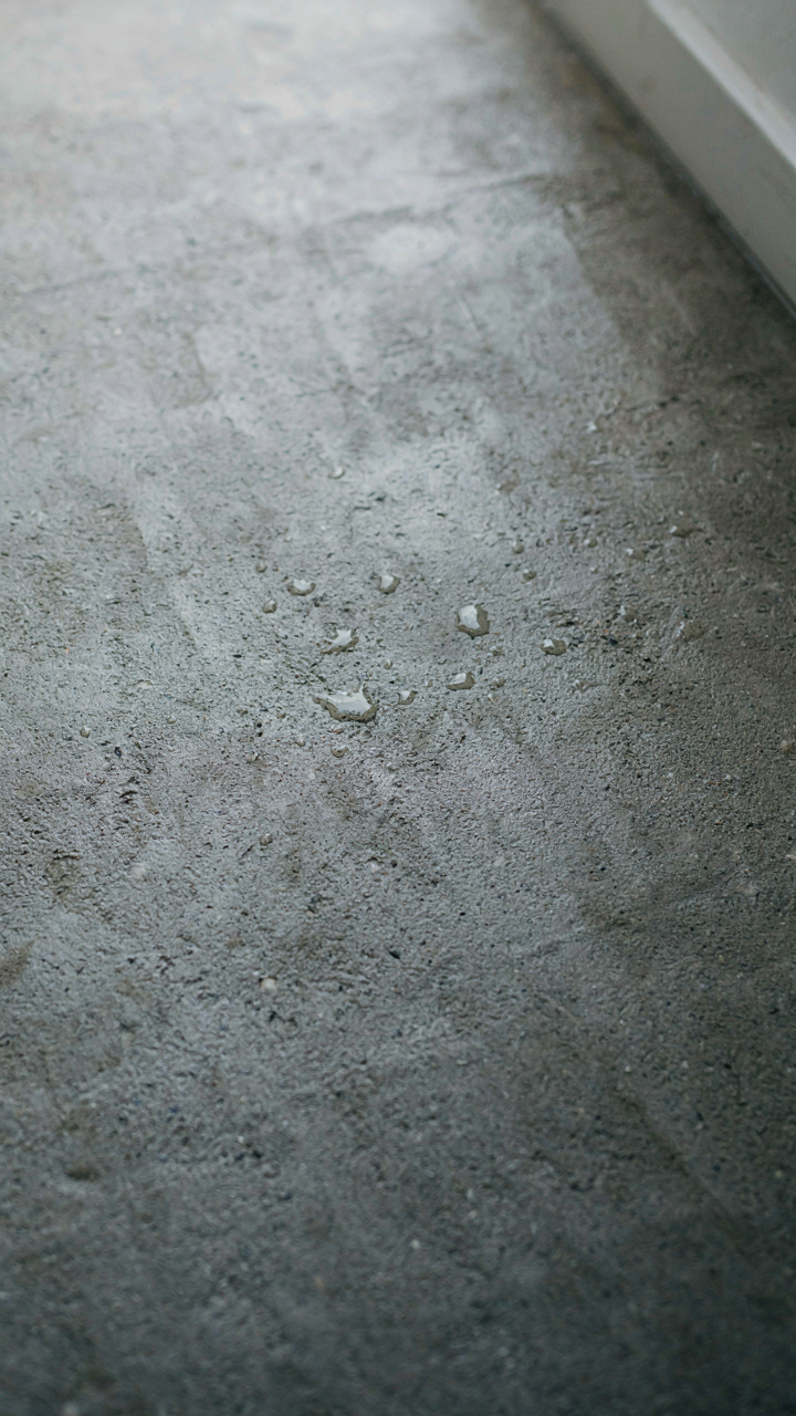 A close-up view of a textured poured concrete bathroom floor with water droplets.