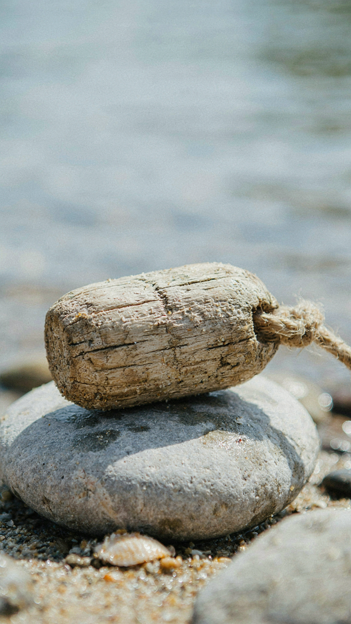 A weathered wooden fishing net float rests on a smooth grey river stone.