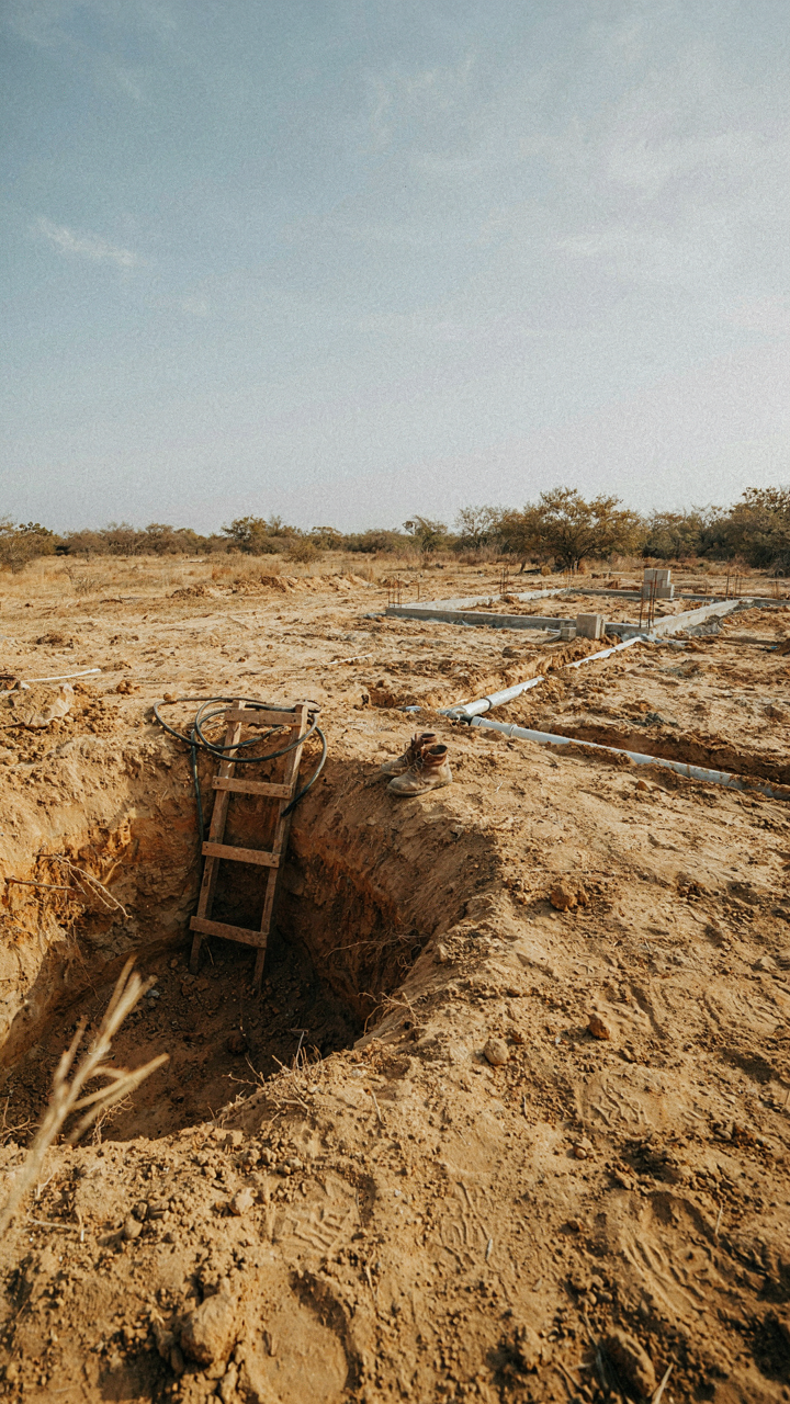 A newly dug well and septic pipes are visible on a rural building site.