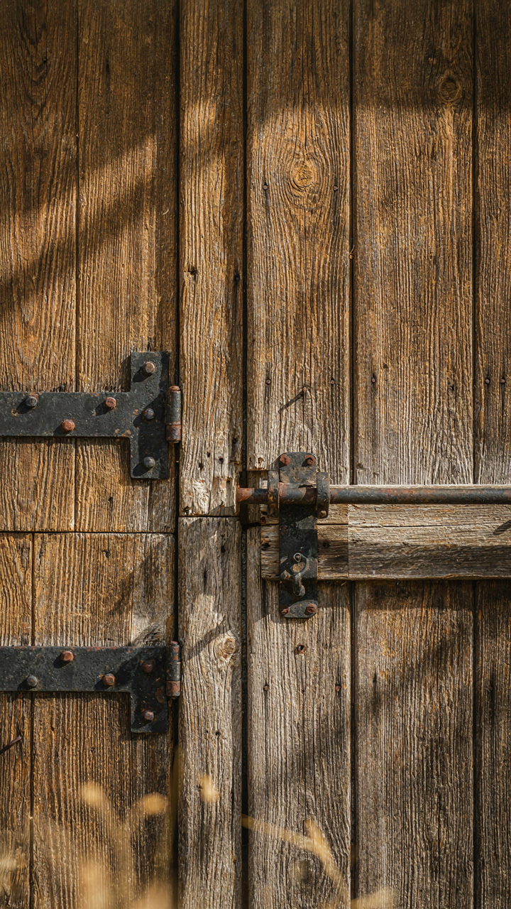 A close-up of a weathered wooden barn door with sturdy metal hinges.