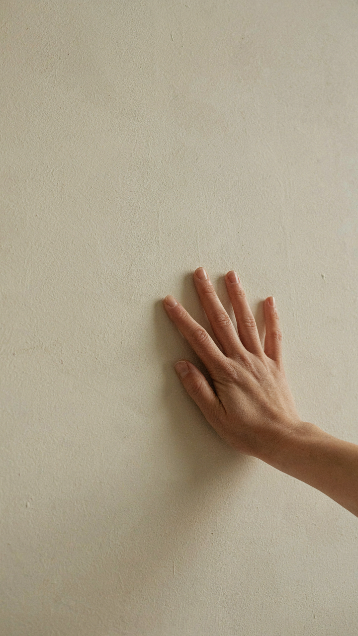 A hand touches a matte cream wall, showing how light reflects to create warmth in cottage lighting.