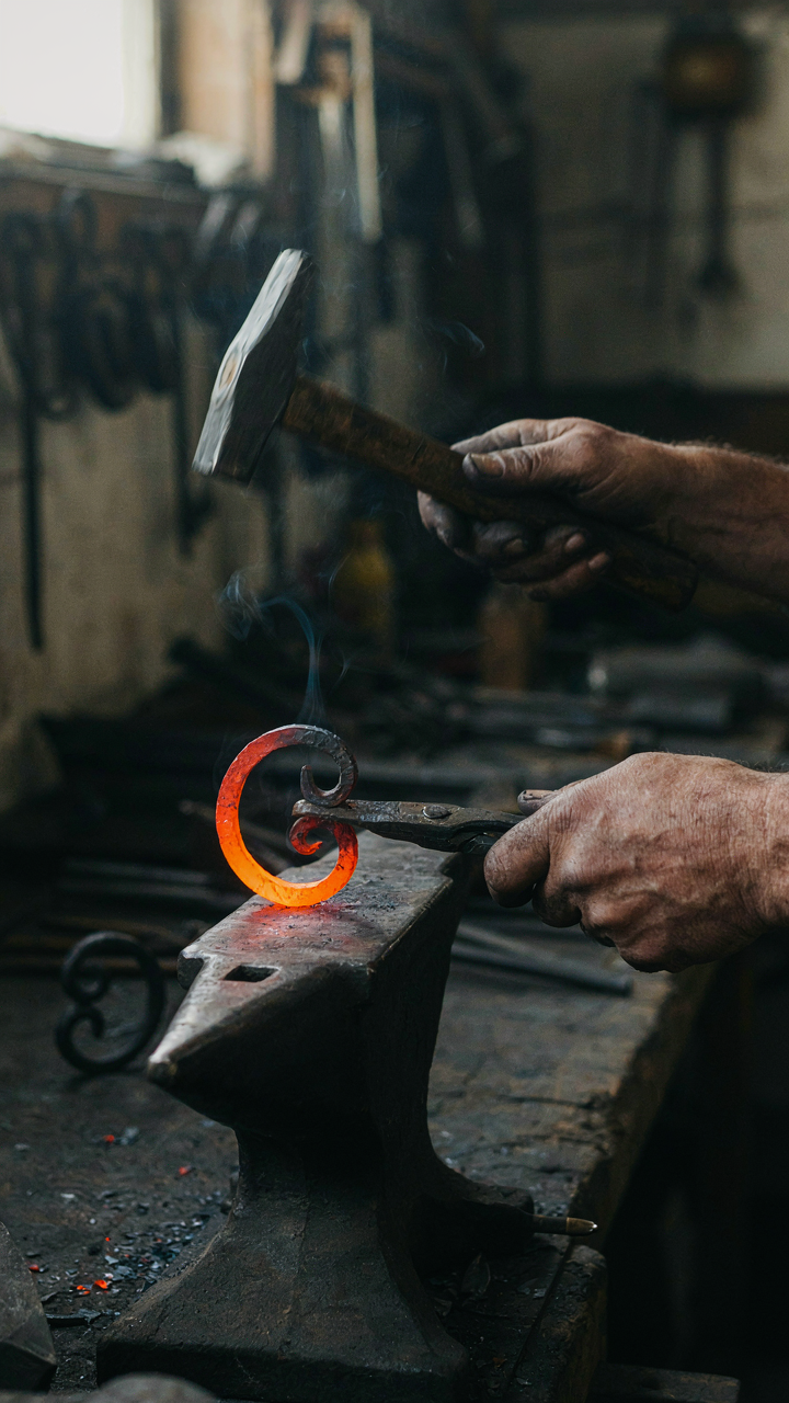 A blacksmith's hands work to shape hot iron for a decorative balcony railing.
