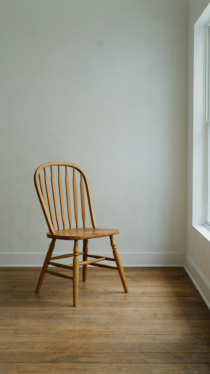 A single wooden Windsor chair in a sparse, bright room.
