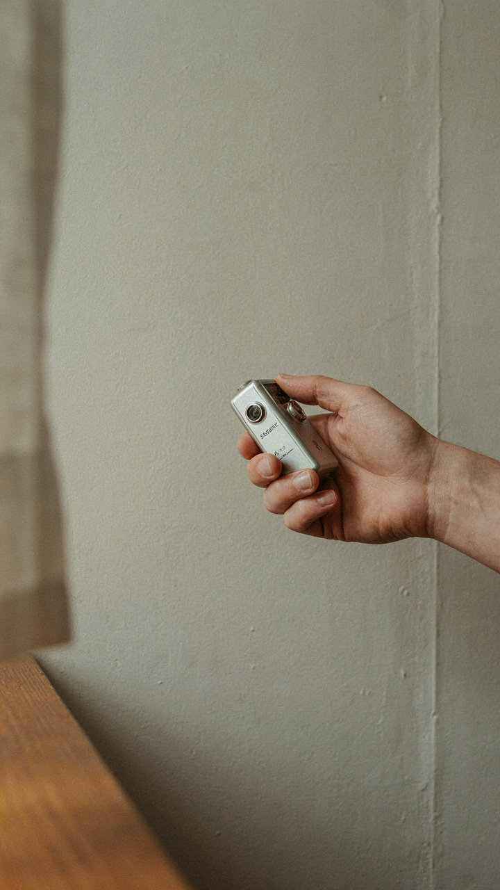 A hand measures light reflectance on a matte plaster wall in a bright room.
