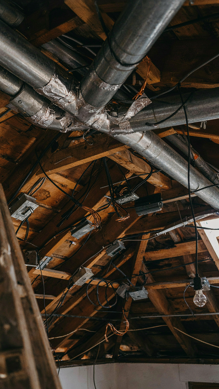 Exposed, haphazard ducts and wires clutter a small cottage loft ceiling.