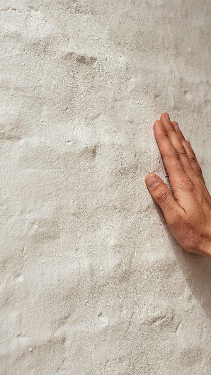 A hand gently touches a subtly textured limewashed white cottage wall.