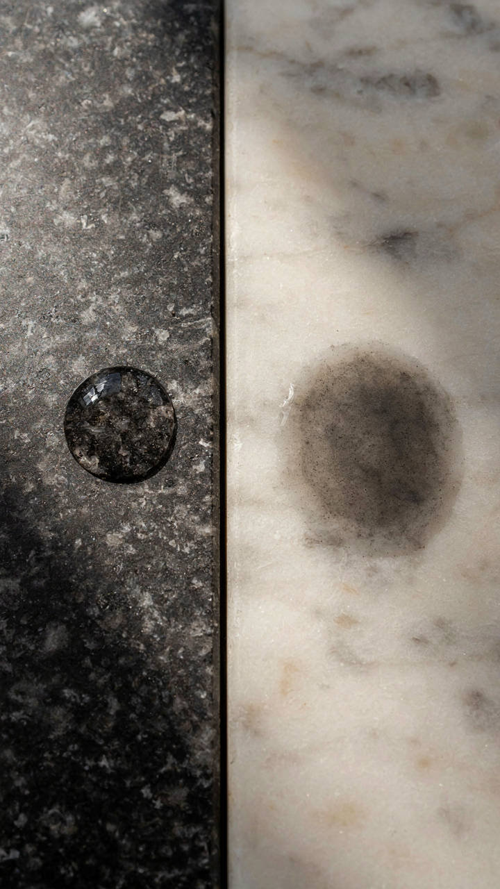 Water beads on sealed granite next to stained marble, showing moisture absorption.
